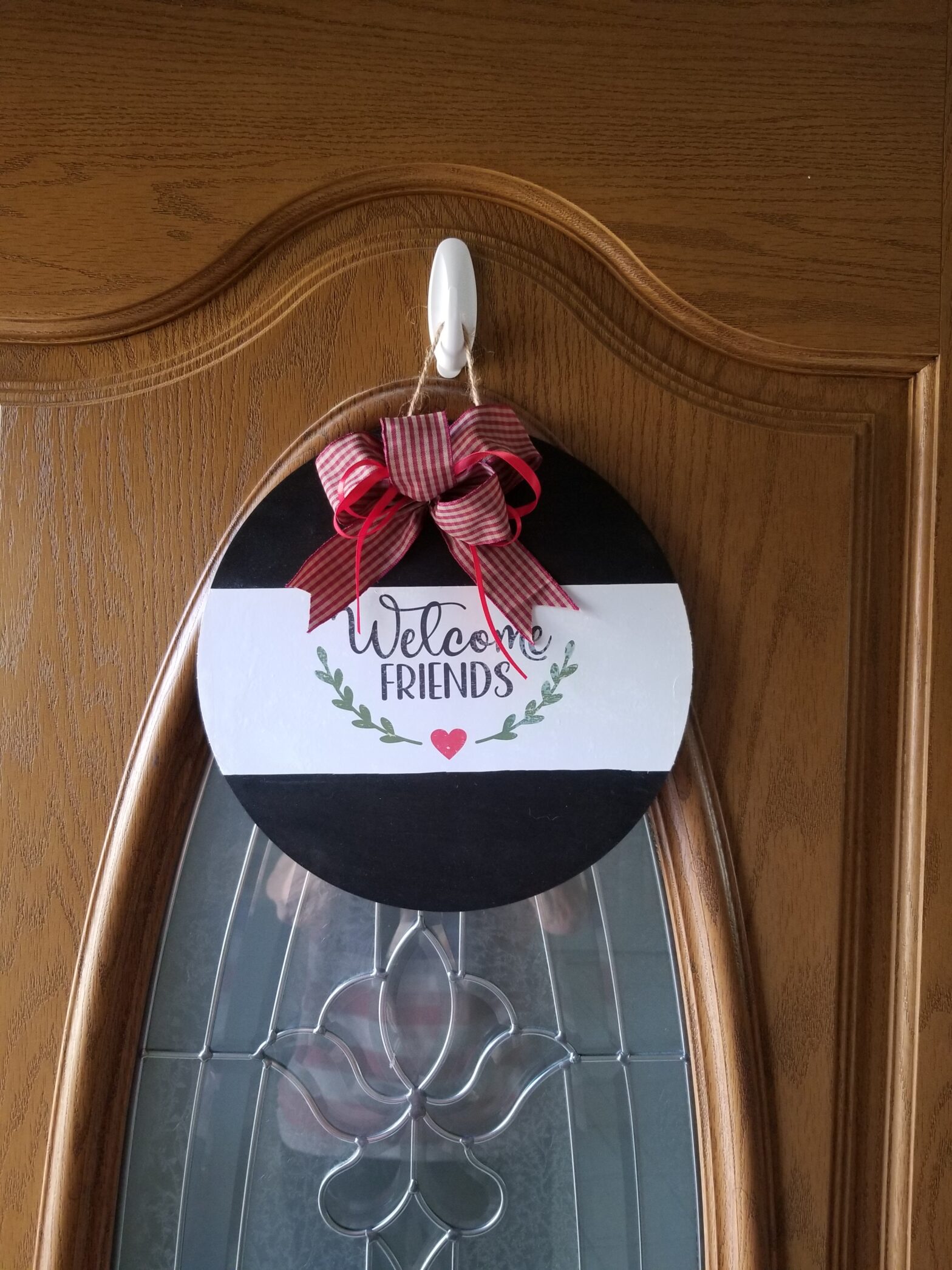 Decorative welcome sign with a red bow hanging on a wooden door.