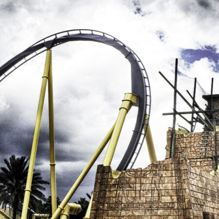 A yellow roller coaster with a steep loop against a cloudy sky.
