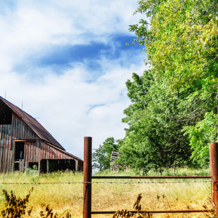 Rustic barn beside a wooden fence under a blue sky.